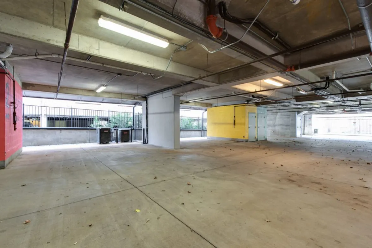 A brightly lit, functional indoor garage space with distinctive red and yellow walls, open space for parking, and areas for vehicle or bicycle storage. The space is uncluttered and designed for practical use, emphasizing ease of access for residents and guests.