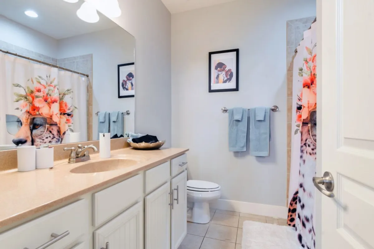 A bathroom with a vibrant shower curtain adorned with floral and animal motifs, a vanity with a sink and counter, and framed art on the walls. The space is playful yet functional, supporting daily routines.
