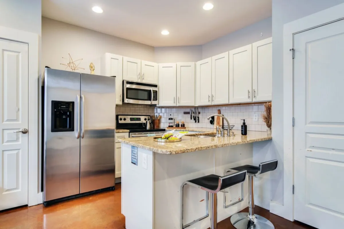 A modern kitchen space featuring a gleaming stainless steel refrigerator, granite countertops, and a breakfast bar with stools. The area is inviting and set up for both family breakfasts or casual meals before heading out to explore.