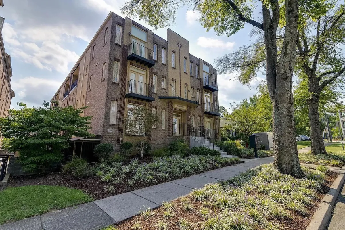 This exterior image showcases the property's modern brick architecture with multiple balconies overlooking lush greenery. The scene includes a sidewalk where residents might stroll out into the vibrant city, as well as inviting communal spaces that evoke a lively neighborhood spirit.