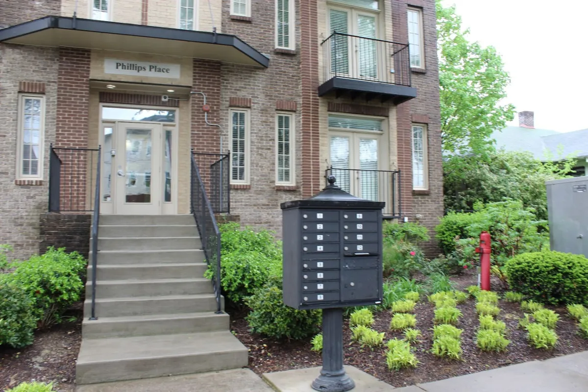 An inviting view of the building's entrance, complete with landscaped gardens, stairs, and a mailbox—suggesting a welcoming return after a night out. The image emphasizes the transition between the energy of the city and the comfort of home.