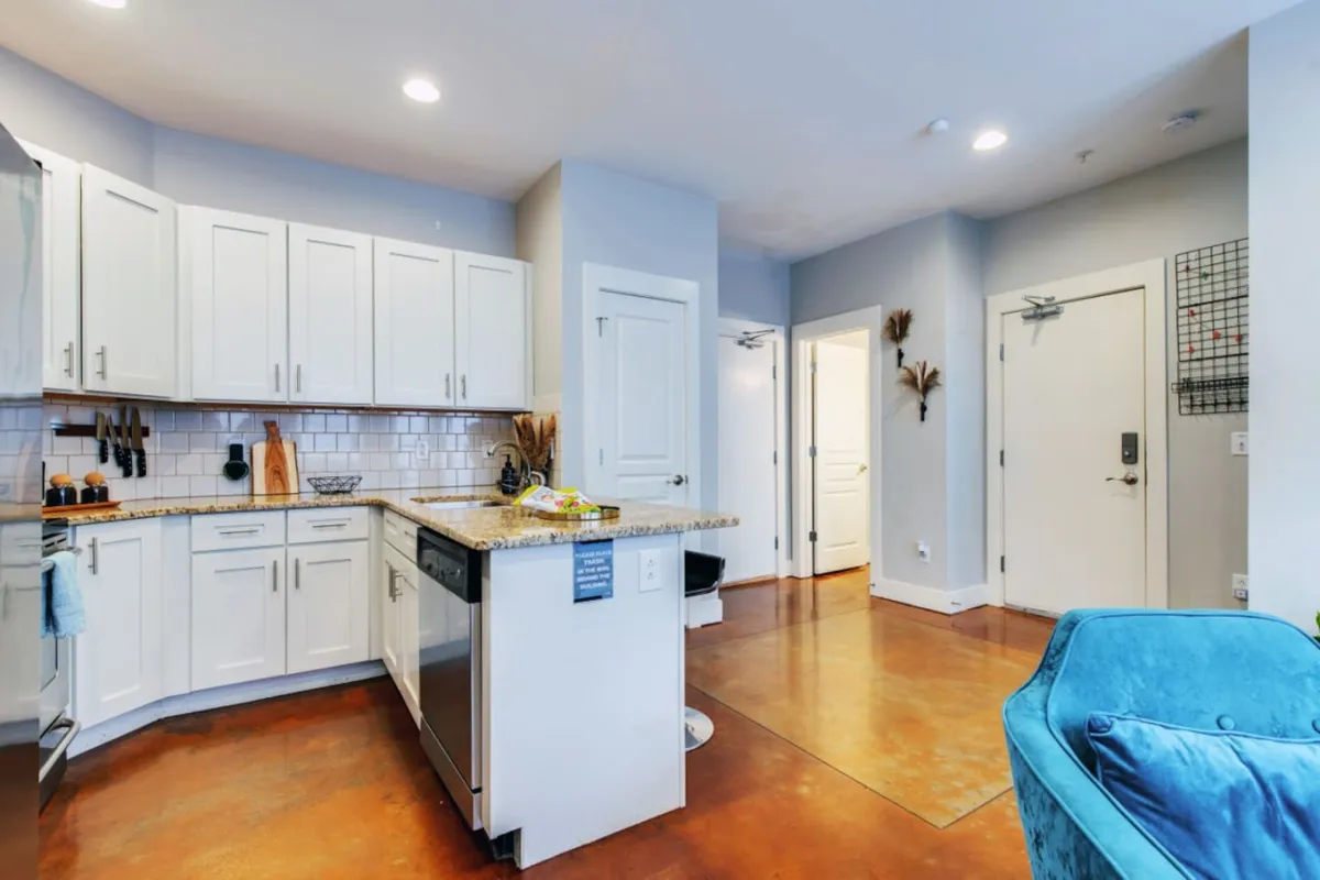 A modern kitchen with a central island, sleek white cabinetry, a granite countertop, and a blue chair. The space is warm and welcoming, ideal for preparing meals or hosting brunches with friends.